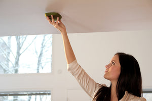 A close up image of a young woman gently installing the KUPU smoke alarm by easily placing it to the ceiling. 