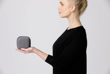 A side view of a woman holding a KUPU smoke alarm to show the size. The smoke alarm, while resting on its side, fits in the palm of the woman's hand. 